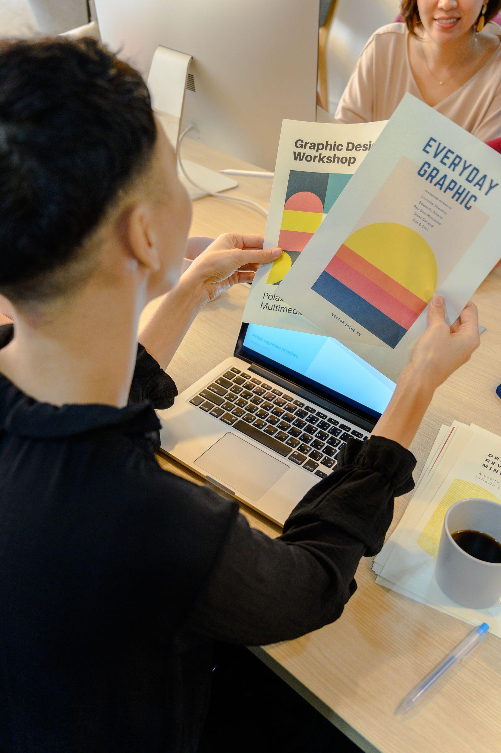 Professional reviewing colorful printed multilingual brochures beside a laptop